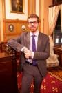 Garrett Hinck in a suit leaning against a mahogany table 