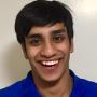 Ayan Mandal, wearing a blue shirt, smiling, and standing in front of a white wall