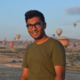 Ridwan Meah, wearing black glasses and an olive shirt, standing in front of hot air ballons