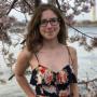 Sophia Griffith standing by the Tidal Basin, wearing glasses and a dress, with cherry blossoms in the background of the photo