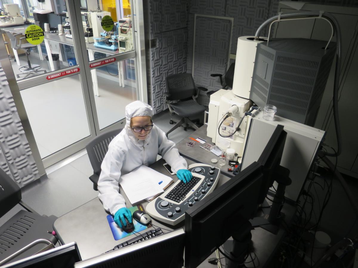 person sitting at a desk in a bunny suit in a lab at a computer surrounded by equipment