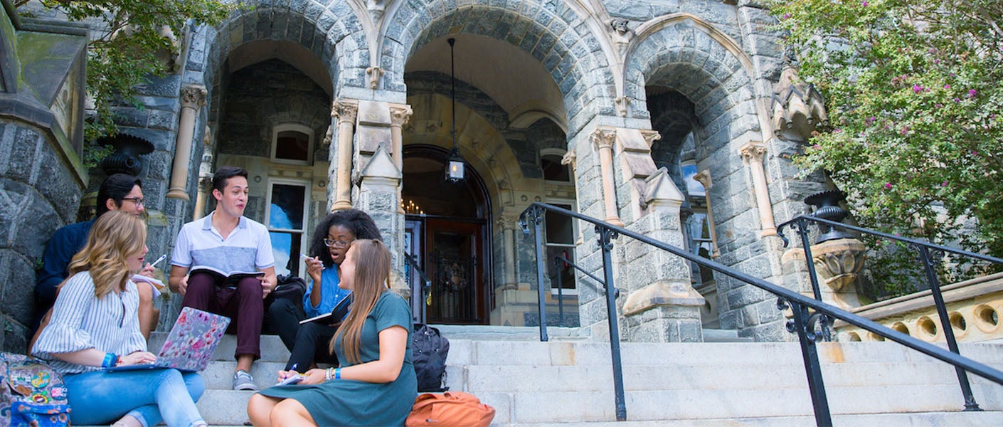 students sitting at the steps of healy hall