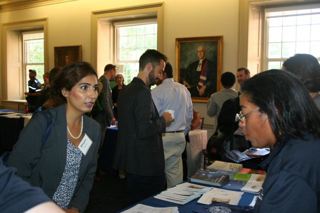 CETS staff standing behind a table at New Faculty Orientation in 2016 with form, a presentation, and free goodies talking to a faculty member about CETS