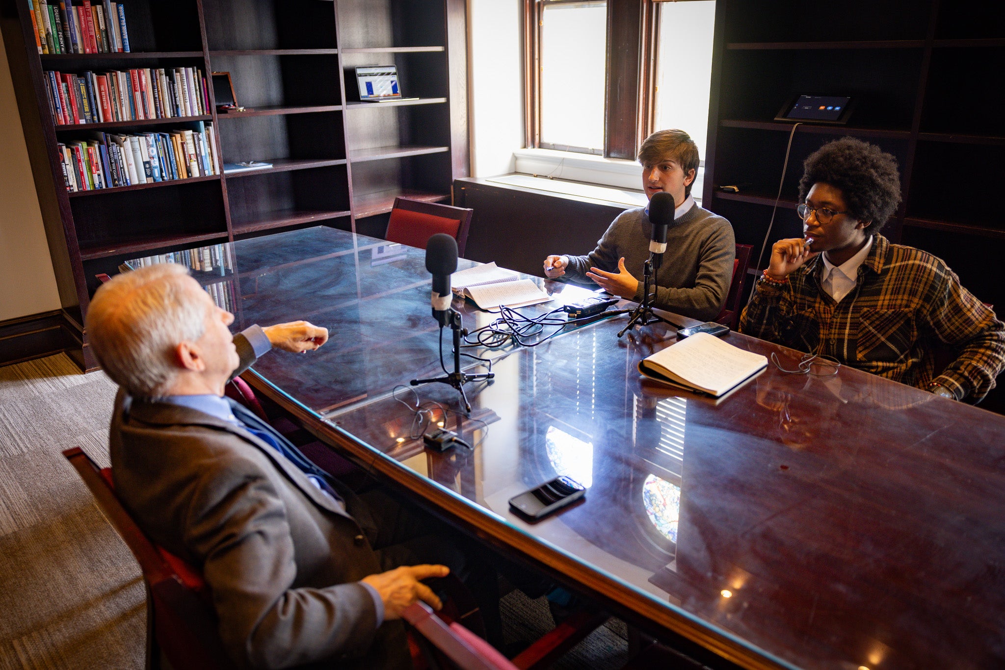 Students sit across from table with Anthony Fauci. Microphones are set up for an interview.