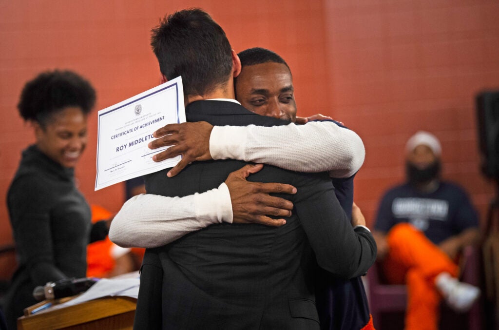 Prison Scholar Roy holds a certificate and hugs PJI Director Marc Howard.