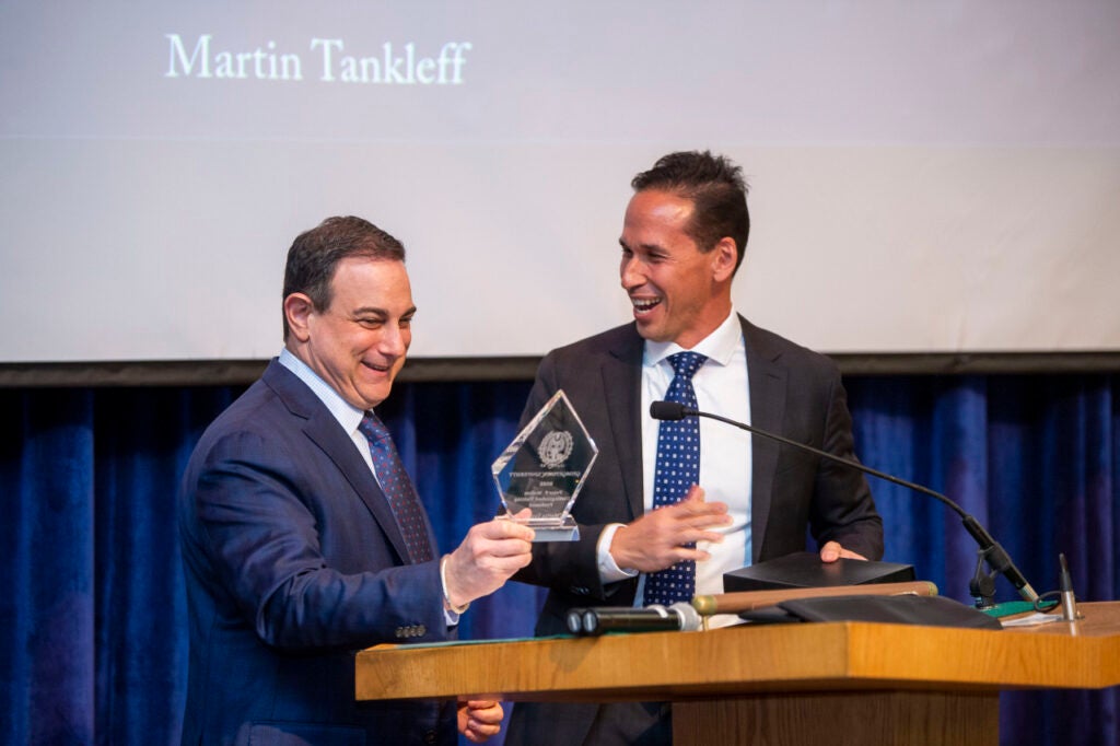 Marc Howard and Martin Tankleff laugh at a podium. Tankleff holds up a glass award.