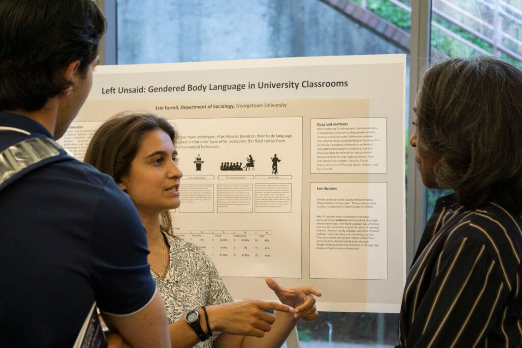 Senior Erin Farrell discusses their presentation with Professor Karolyn Tyson and another community member, gesturing with their hands