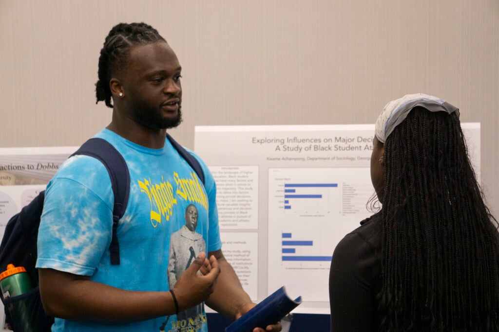 Senior Kwame Achampong discusses their presentation with a community member, gesturing with their hands