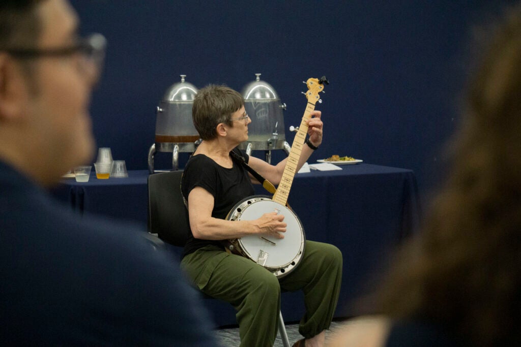 Professor Sarah Stiles performs a song on the banjo while seated